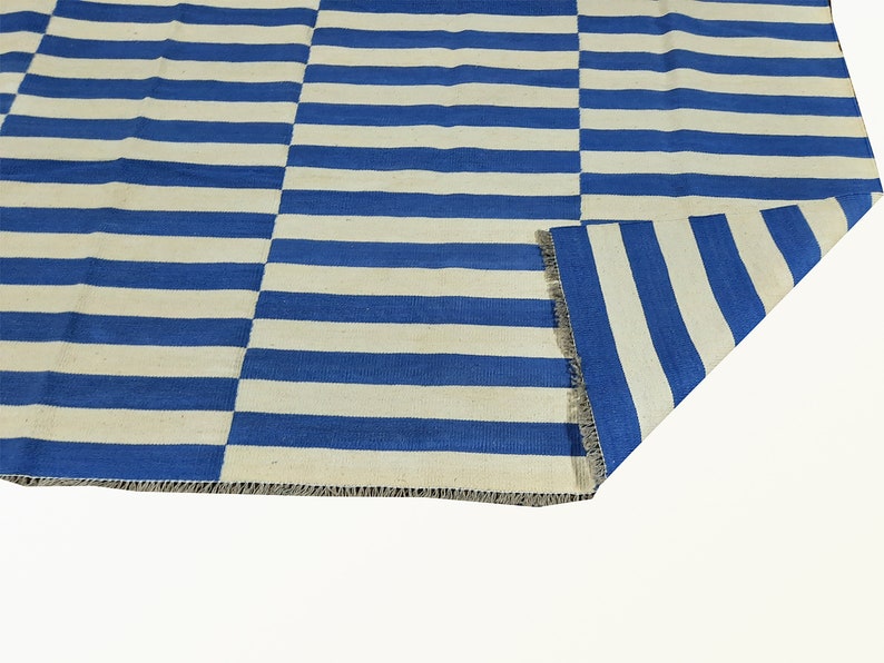 May include: A blue and white striped rug with a woven texture. The rug is folded in half, showing the fringe on the edge.