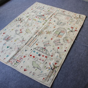 以下が含まれることがあります： カラフルな刺繍模様が施された白い綿の敷物。敷物には、鳥、蝶、花、幾何学模様が描かれています。