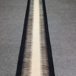 May include: A long, narrow runner rug with a white center stripe and black and gray chevron patterns on either side.