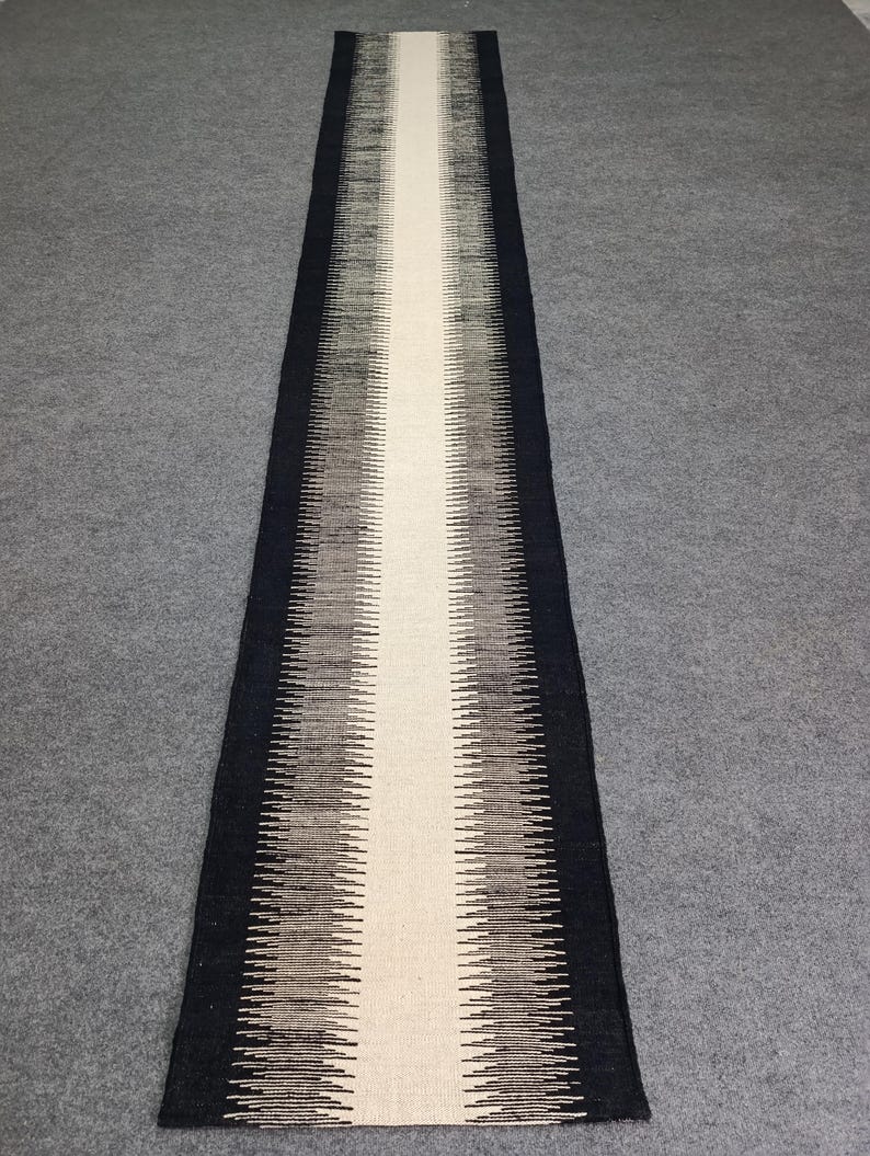 May include: A long, narrow runner rug with a white center stripe and black and gray chevron patterns on either side.