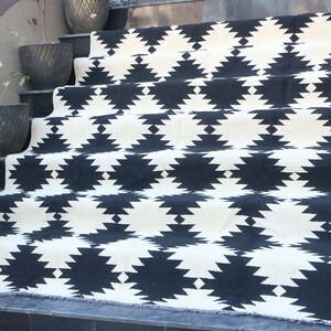 Puede incluir: Alfombra geom&eacute;trica de patr&oacute;n blanco y negro con borde de flecos. La alfombra est&aacute; colocada en un conjunto de escaleras.