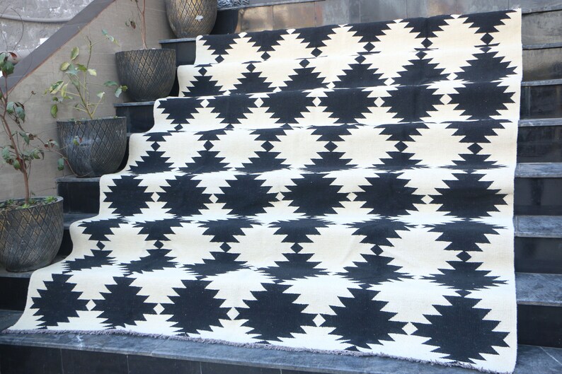 Puede incluir: Alfombra geom&eacute;trica de patr&oacute;n blanco y negro con borde de flecos. La alfombra est&aacute; colocada en un conjunto de escaleras.