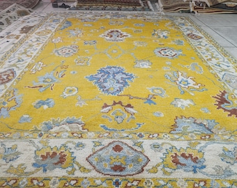 Könnte beinhalten: Ein großer, rechteckiger Teppich mit einem leuchtend gelben Mittelfeld. Der Teppich weist ein detailliertes Blumenmuster in Blau-, Weiß- und Brauntönen auf. Der Rand ist cremefarben mit sich wiederholenden Blumenmotiven. Der Teppich ist wahrscheinlich aus Wolle.