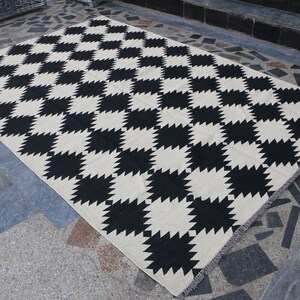 Puede incluir: Alfombra a cuadros negros y blancos con un patr&oacute;n geom&eacute;trico. La alfombra tiene un borde de flecos.