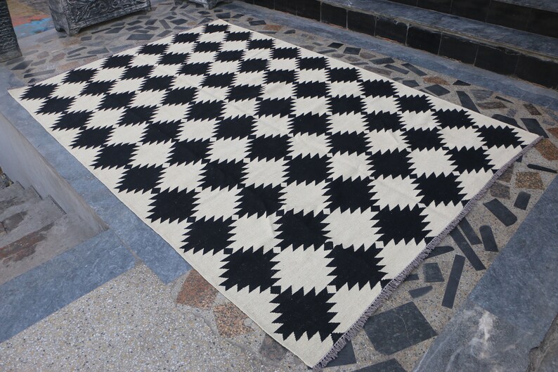 Puede incluir: Alfombra a cuadros negros y blancos con un patr&oacute;n geom&eacute;trico. La alfombra tiene un borde de flecos.