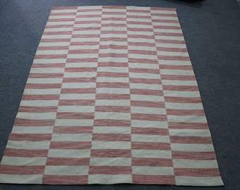 May include: A large, rectangular rug with a checkered pattern in shades of red and white. The rug is made of a woven material and has a slightly textured surface.