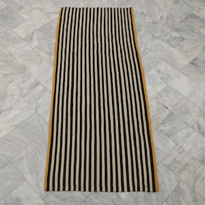 May include: A black and white striped runner rug with a yellow border. The rug is on a gray marble floor.