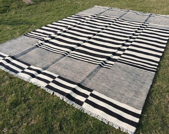 Puede incluir: Alfombra de rayas blancas y negras con un patrón geométrico. La alfombra tiene un borde de flecos y está hecha de un material tejido.