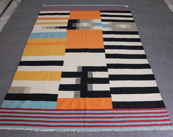 May include: A colorful geometric rug with black, white, orange, yellow, and blue stripes and blocks. The rug has a fringe border.