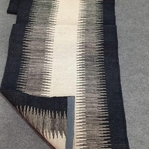 May include: A black and white striped runner rug with a white center stripe. The rug has a fringe border and is made of a soft, woven material.