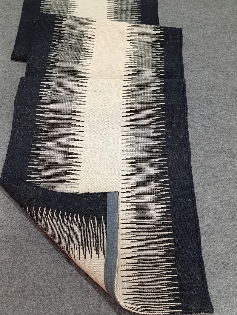 May include: A black and white striped runner rug with a white center stripe. The rug has a fringe border and is made of a soft, woven material.