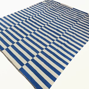 May include: A blue and white striped rug with a checkered pattern. The rug is made of a soft, woven material and has a fringed edge.