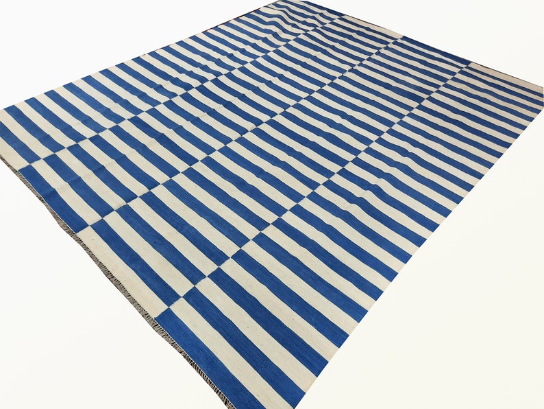 May include: A blue and white striped rug with a checkered pattern. The rug is made of a soft, woven material and has a fringed edge.