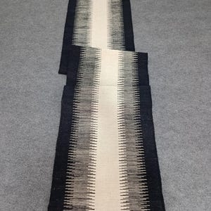 May include: A black and white striped runner rug with a white center stripe. The rug is made of a woven material and has a subtle sheen.