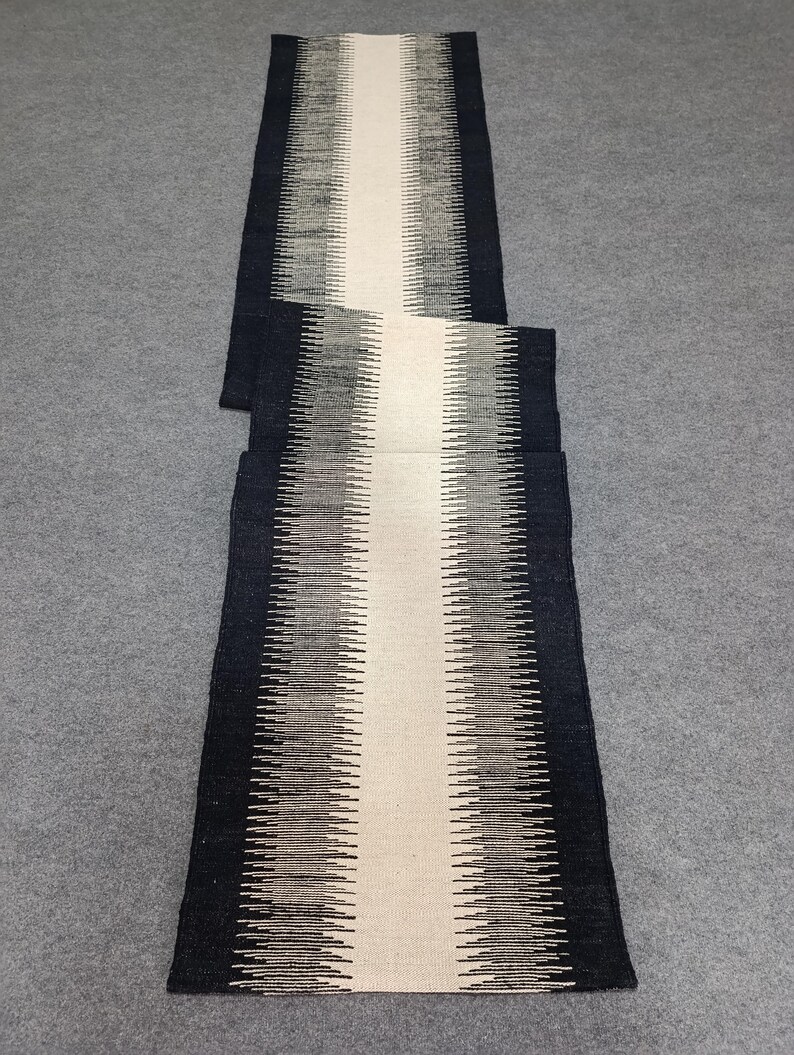 May include: A black and white striped runner rug with a white center stripe. The rug is made of a woven material and has a subtle sheen.