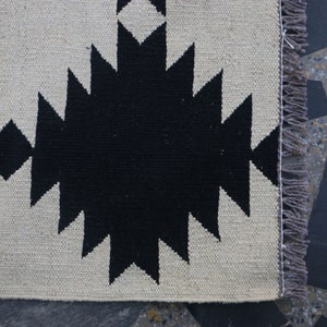Puede incluir: Alfombra de patr&oacute;n geom&eacute;trico en blanco y negro con flecos en el lado derecho.