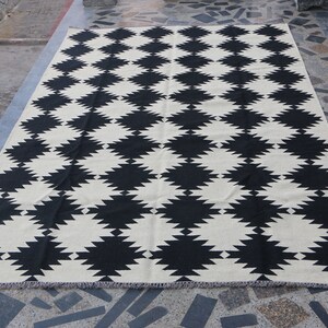 Puede incluir: Alfombra geom&eacute;trica con estampado en blanco y negro con dise&ntilde;o de rombos. La alfombra tiene un borde con flecos.