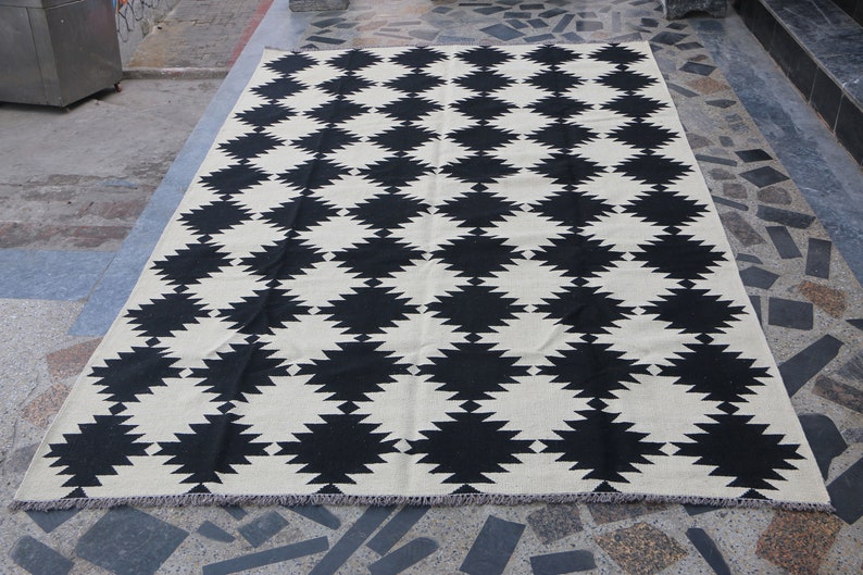 Puede incluir: Alfombra geom&eacute;trica con estampado en blanco y negro con dise&ntilde;o de rombos. La alfombra tiene un borde con flecos.