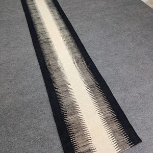 May include: A black and white runner rug with a geometric pattern. The rug has a long, narrow shape and is made of a soft, woven material.