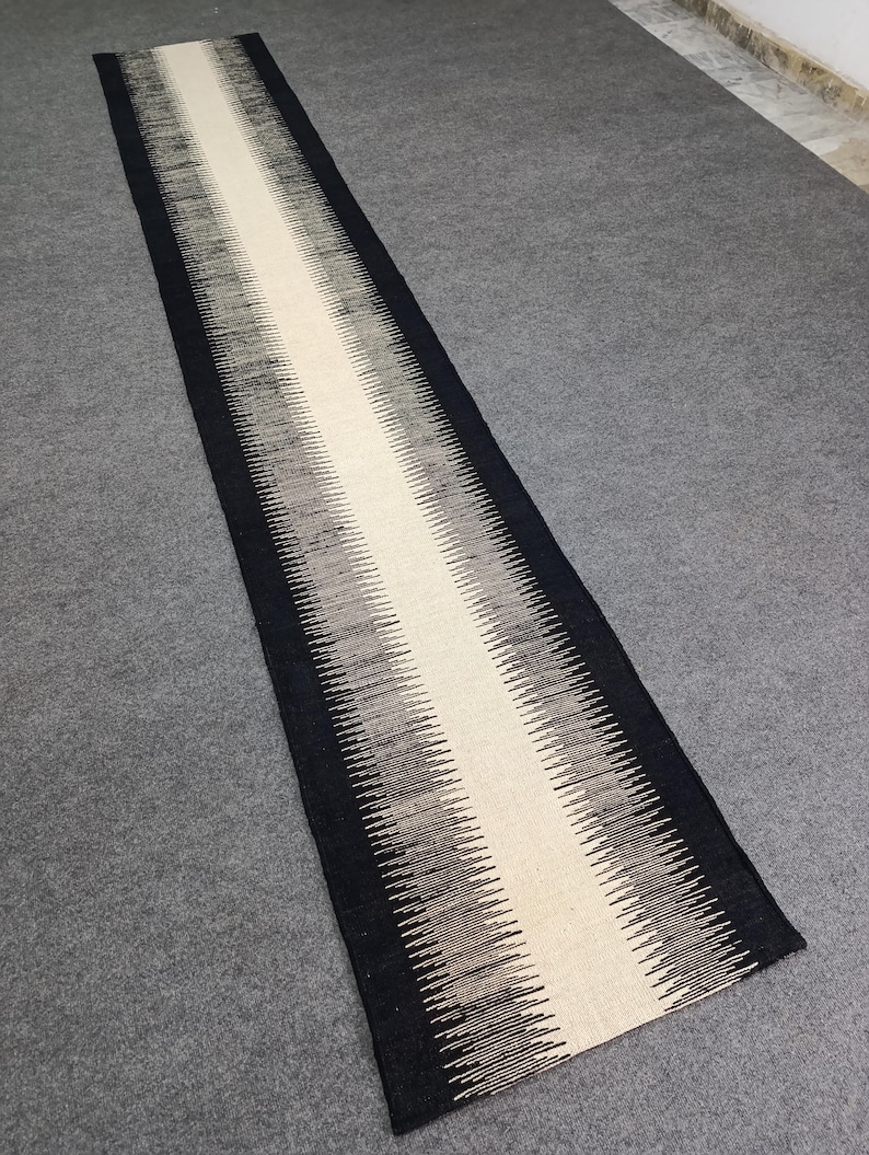 May include: A black and white runner rug with a geometric pattern. The rug has a long, narrow shape and is made of a soft, woven material.