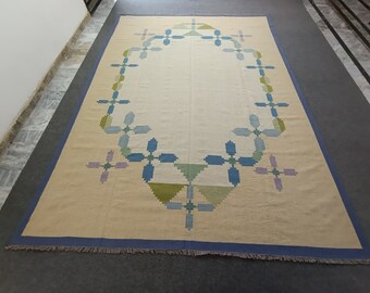 May include: A beige rug with a blue, green, and purple geometric pattern. The pattern features a repeating flower design around the perimeter of the rug.