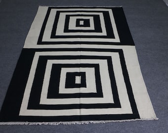 Puede incluir: Alfombra geométrica en blanco y negro con un patrón de cuadrados concéntricos. La alfombra tiene un borde de flecos.
