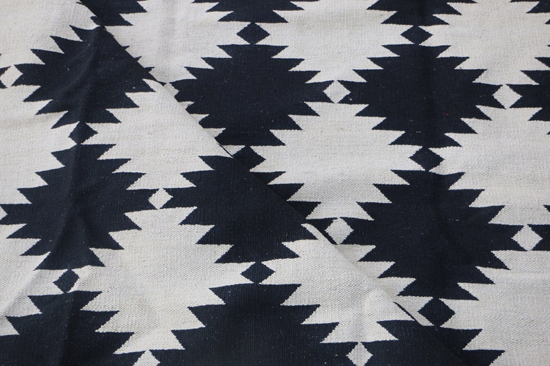 Puede incluir: Tela con estampado geom&eacute;trico en blanco y negro con un patr&oacute;n de rombos. La tela est&aacute; doblada por la mitad, mostrando el patr&oacute;n en ambos lados.