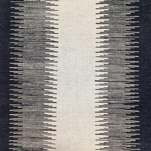 May include: Black and white striped rug with a textured woven design. The rug has a central white stripe with black stripes on either side.