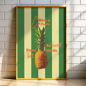 May include: A framed art print featuring a pineapple illustration with the words "Wear a Crown, Stand Tall, Be Sweet Inside" in orange script. The background has green and cream vertical stripes.