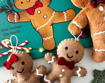 May include: A festive image featuring a children's book titled "FRED" with a gingerbread man illustration. Accompanying the book are several gingerbread man ornaments with red bowties and white icing details, perfect for holiday decor.