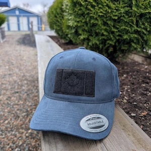 May include: A navy blue adjustable baseball cap with a black maple leaf patch. The cap has a curved peak and a white sticker that reads "THE AUTHENTIC ADJUSTABLE".