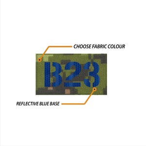 Könnte beinhalten: Ein Tarnstoff-Patch mit dem Text "B23" in blauen reflektierenden Buchstaben. Der Patch hat eine reflektierende blaue Basis und die Farbe des Stoffes kann angepasst werden.