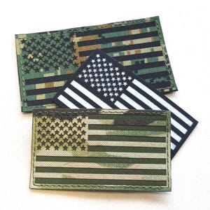 Peut inclure: Trois écussons rectangulaires avec des motifs de drapeau américain. L'un est noir et blanc, un autre présente un motif de camouflage vert et marron, et le troisième un motif de camouflage vert et beige.