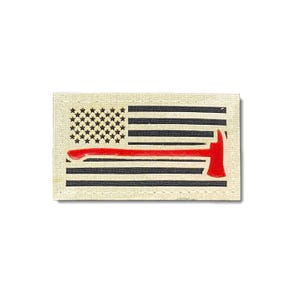 Può includere: Un cerotto in tessuto beige con un design di bandiera americana rosso, bianco e blu. Un'ascia rossa dei vigili del fuoco è sovrapposta alla bandiera, con il manico dell'ascia che corre orizzontalmente attraverso la bandiera.