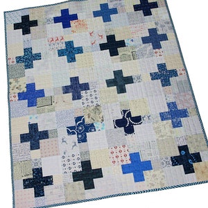 Może przedstawiać: Kołdra patchworkowa z białym tłem i niebieskimi i czarnymi znakami plus. Kołdra jest wykonana z różnych tkanin o różnych wzorach i fakturach.