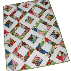 Può includere: Una trapunta colorata con un motivo geometrico di quadrati e triangoli. La trapunta è realizzata con una varietà di tessuti in tonalità di rosso, verde, blu, marrone e bianco. La trapunta è bordata con un bordo verde.