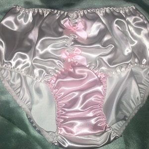 May include: White satin underwear with pink satin trim and bows. The underwear has a ruffled edge.