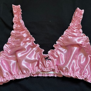 May include: Pink satin lingerie top with ruffled edges and a black bow at the center.