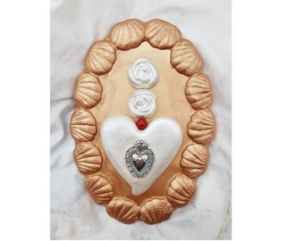 May include: A white heart with a silver heart inside, surrounded by white roses and a red bead. The heart is framed by a gold oval with a border of seashells.