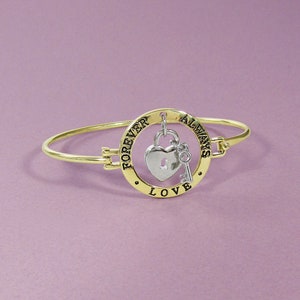 May include: Gold bangle bracelet with a charm that says "Forever Always Love" and features a heart-shaped padlock and a key.