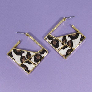 May include: A pair of gold square hoop earrings with a white and brown animal print design.