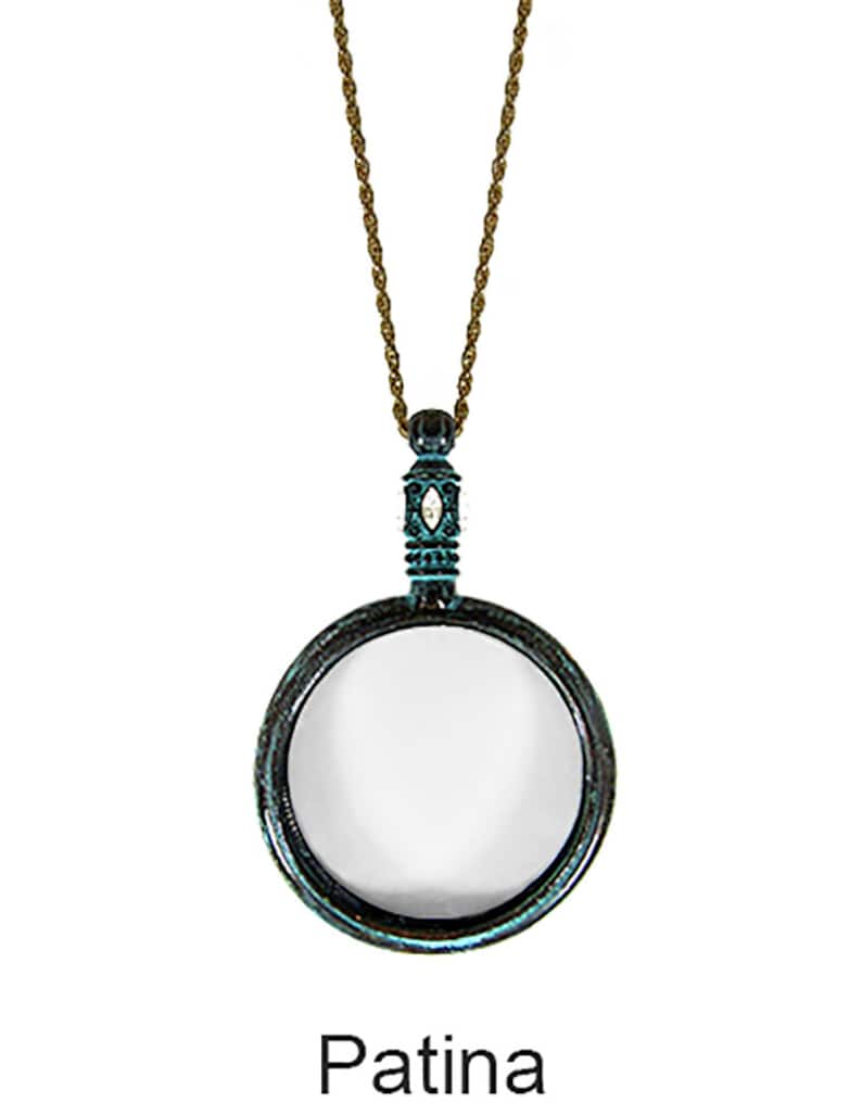 May include: A vintage-style magnifying glass pendant necklace with a bronze-colored chain. The magnifying glass has a circular frame with a teal patina finish. The word "Patina" is printed at the bottom.
