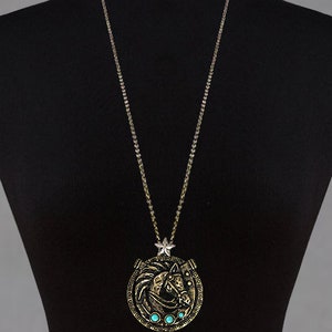 May include: A gold chain necklace with a pendant featuring a horse head design with turquoise stones. The pendant is in the shape of a horseshoe.