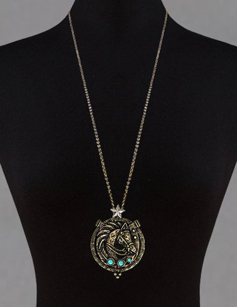 May include: A gold chain necklace with a pendant featuring a horse head design with turquoise stones. The pendant is in the shape of a horseshoe.