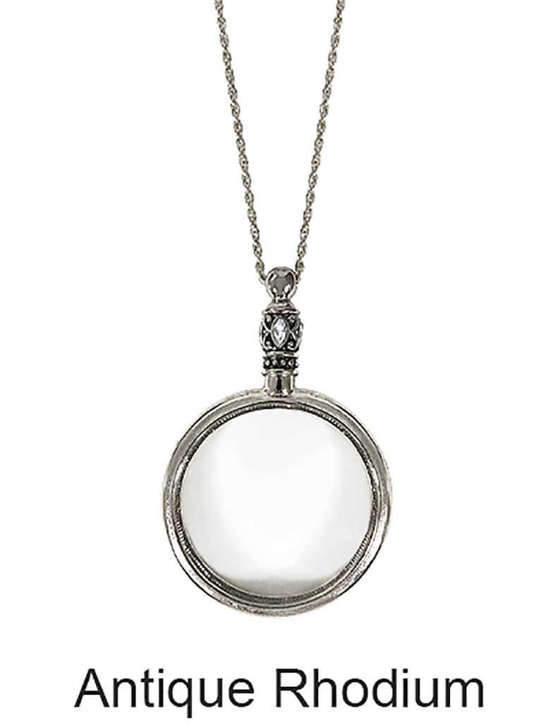 May include: Antique rhodium-plated magnifying glass pendant necklace. The pendant features a circular magnifying glass with a decorative bezel and a detailed bail. The chain is a delicate silver-tone rope style. The text "Antique Rhodium" is at the bottom.