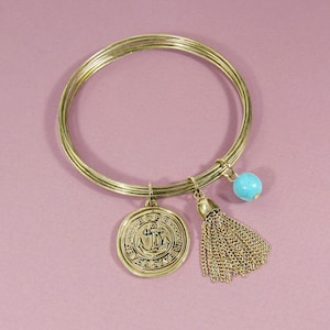 Peut inclure: Bracelet en or avec plusieurs breloques, dont un charme rond avec une ancre et les mots "We've Only Just Begun", une perle turquoise et un pompon doré.