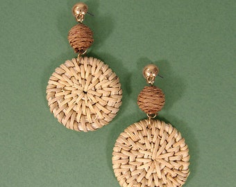 May include: A pair of woven straw earrings with brown wooden beads. The earrings are round and have a natural, rustic look.