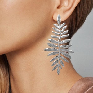 Puede incluir: Pendientes de hoja de plata. Los pendientes son largos y tienen un diseño texturizado.