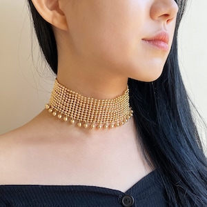 May include: A gold choker necklace with a chainmail design and a fringe of small gold beads.