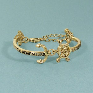 May include: Gold-toned bracelet featuring a charm of an anchor and a ship's wheel. The bracelet is engraved with the words "The Adventure Begins".
